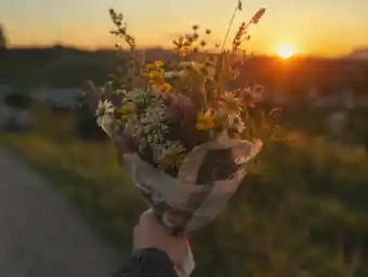 A hand holding wildflowers wrapped in newspaper